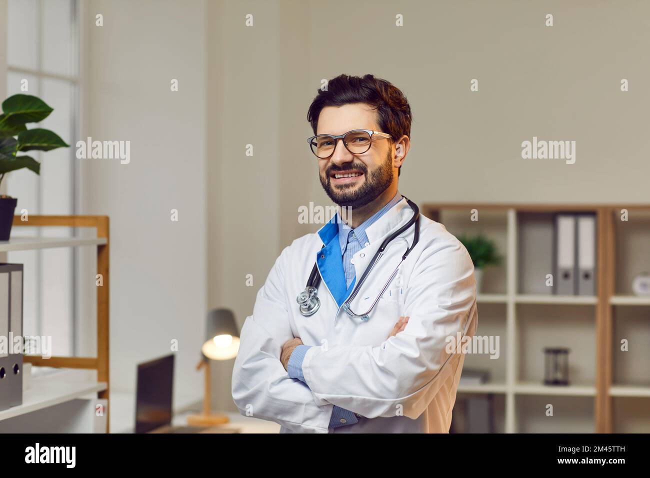Medico sorridente sicuro che posa con le braccia incrociate in ospedale Foto Stock