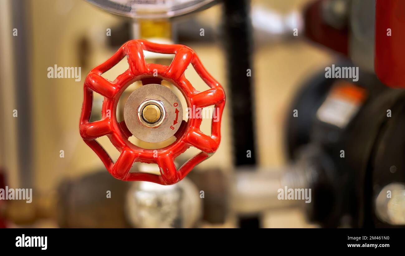 Primo piano della valvola in metallo verniciata di rosso con sfondo sfocato del sistema di tubazioni dell'edificio, messa a fuoco selettiva Foto Stock
