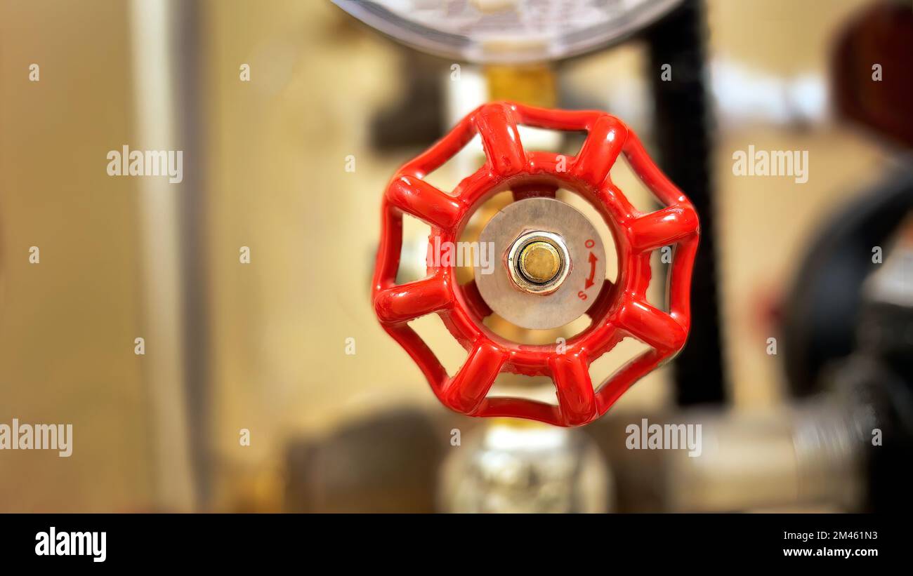 Primo piano della valvola in metallo verniciata di rosso con sfondo sfocato del sistema di tubazioni dell'edificio, messa a fuoco selettiva Foto Stock
