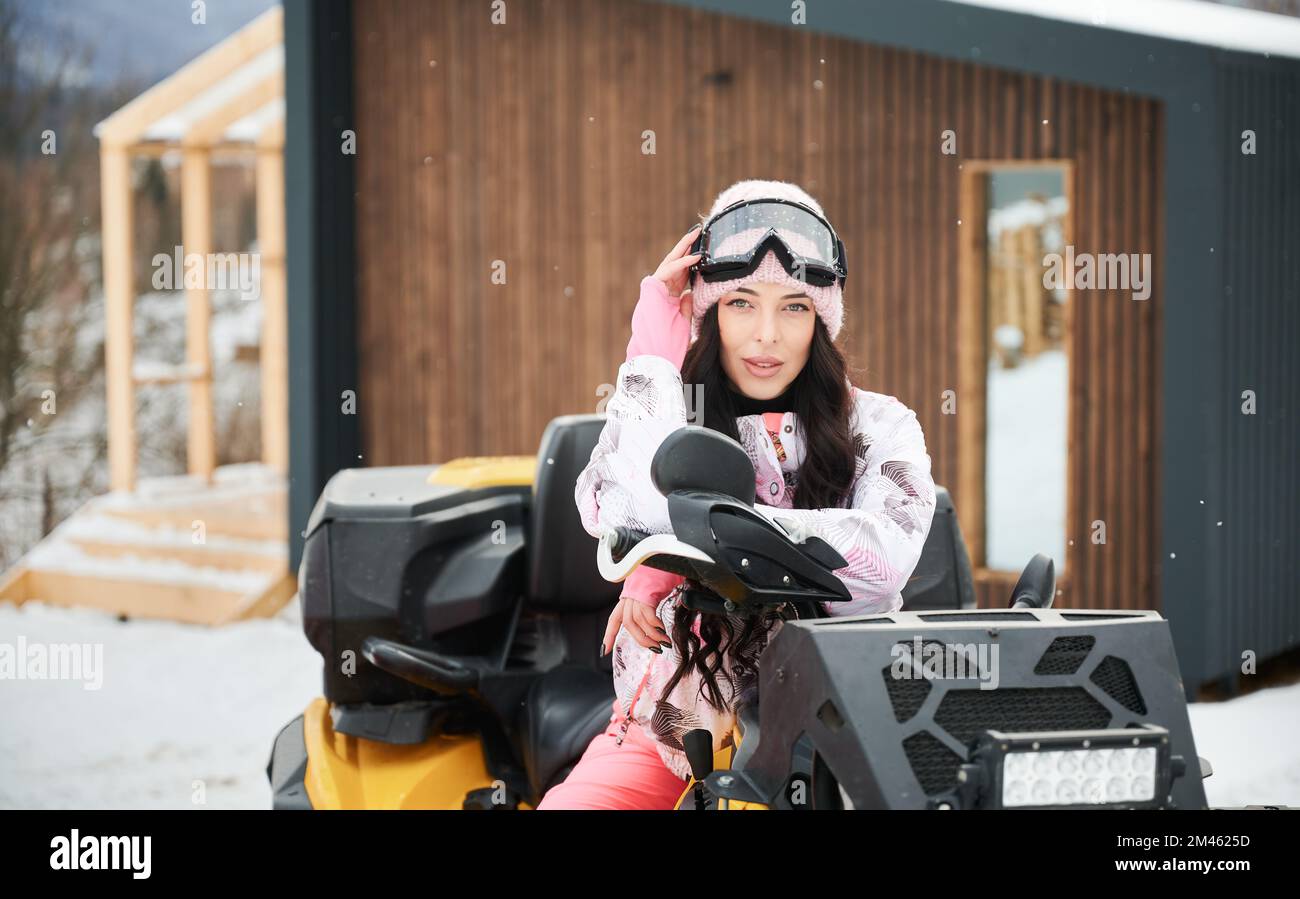 Ritratto di bella donna in posa su fuoristrada quattro ruote ATV con casa in legno su sfondo. Concetto di attività ricreative e invernali. Foto Stock