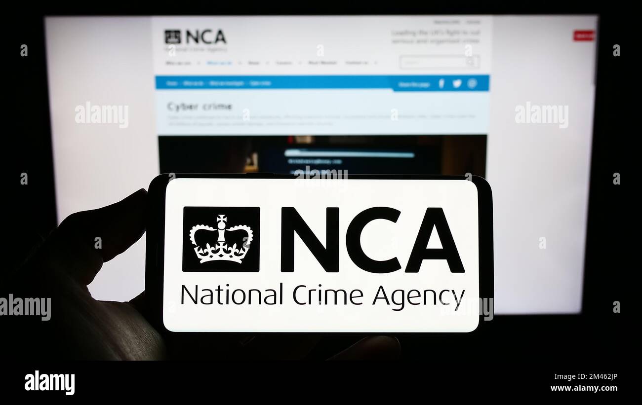 Persona che tiene il cellulare con il logo della British National Crime Agency (NCA) sullo schermo di fronte alla pagina web. Messa a fuoco sul display del telefono. Foto Stock