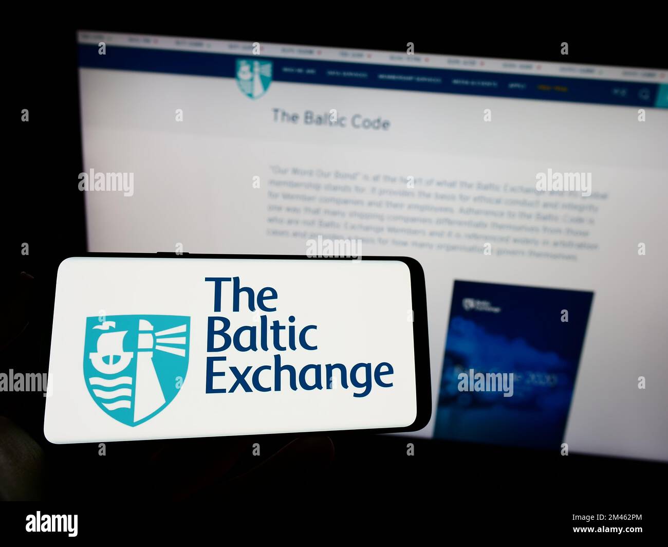 Persona che tiene il cellulare con il logo della società britannica The Baltic Exchange Limited sullo schermo di fronte alla pagina web aziendale. Messa a fuoco sul display del telefono. Foto Stock