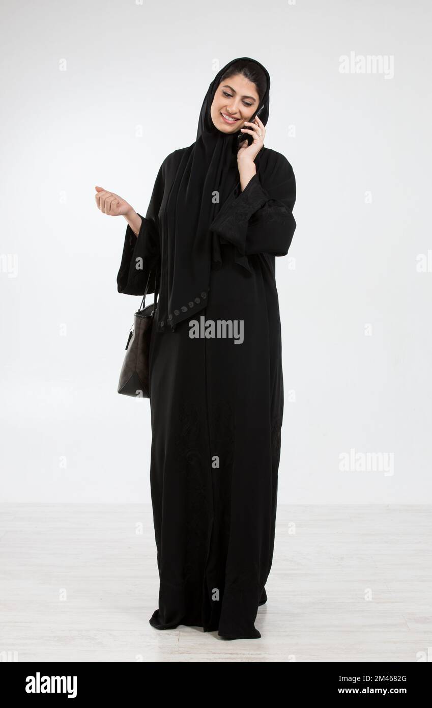 Donna araba che parla al telefono mentre trasporta una borsa. Foto Stock