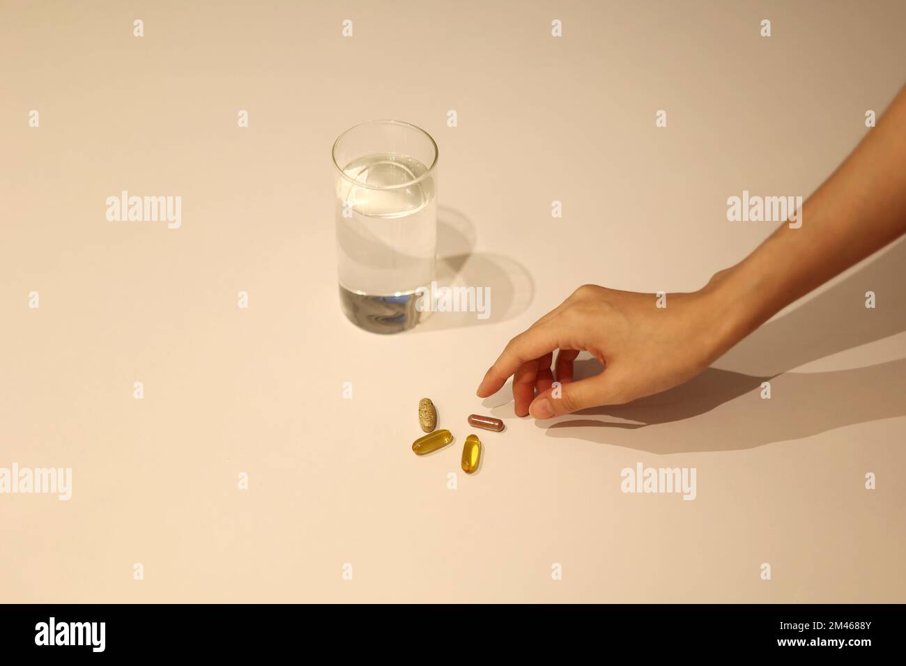 La donna sta prendendo la medicina con la tazza di acqua sulla tabella bianca, la ragazza sta prendendo il supplemento nutrizionale a mano Foto Stock