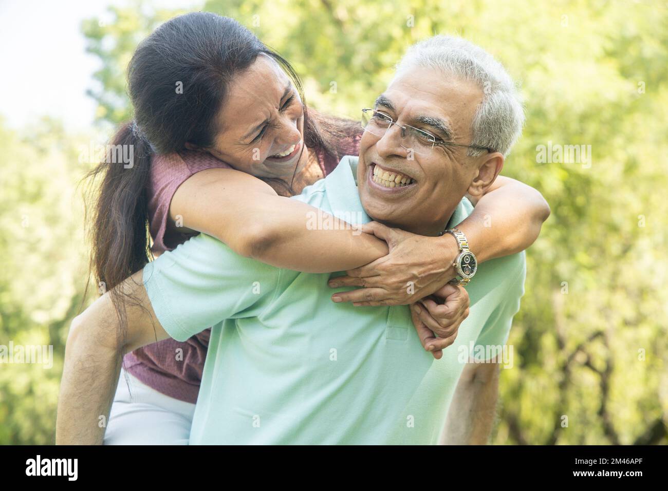 Coppia anziana indiana felice godendo la vita divertirsi al parco estivo, l'uomo che dà piggyback corsa a donna. Foto Stock