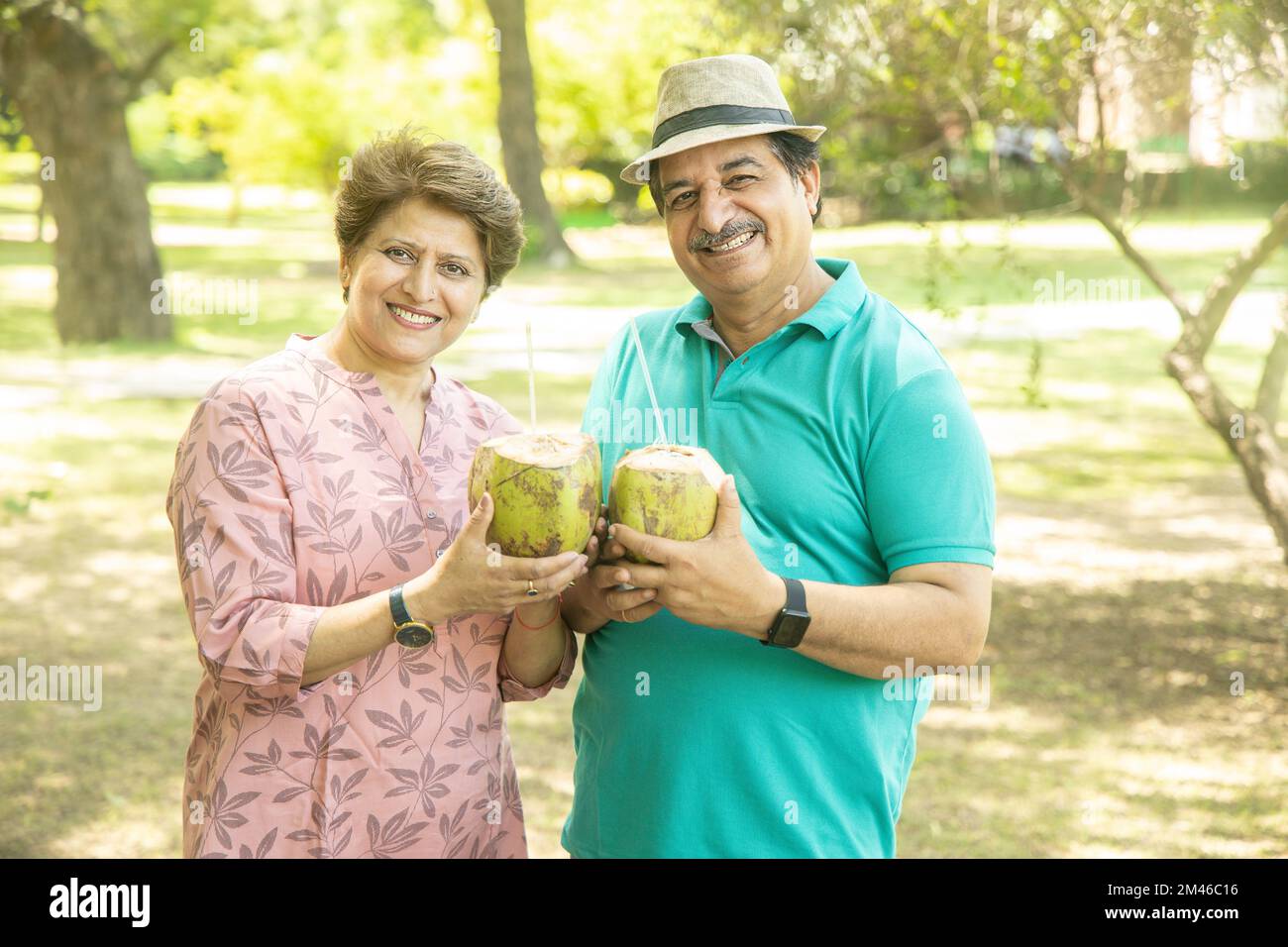 Felice coppia indiana senior con acqua di cocco al parco estivo. Anziani che godono di vita di pensione. Foto Stock