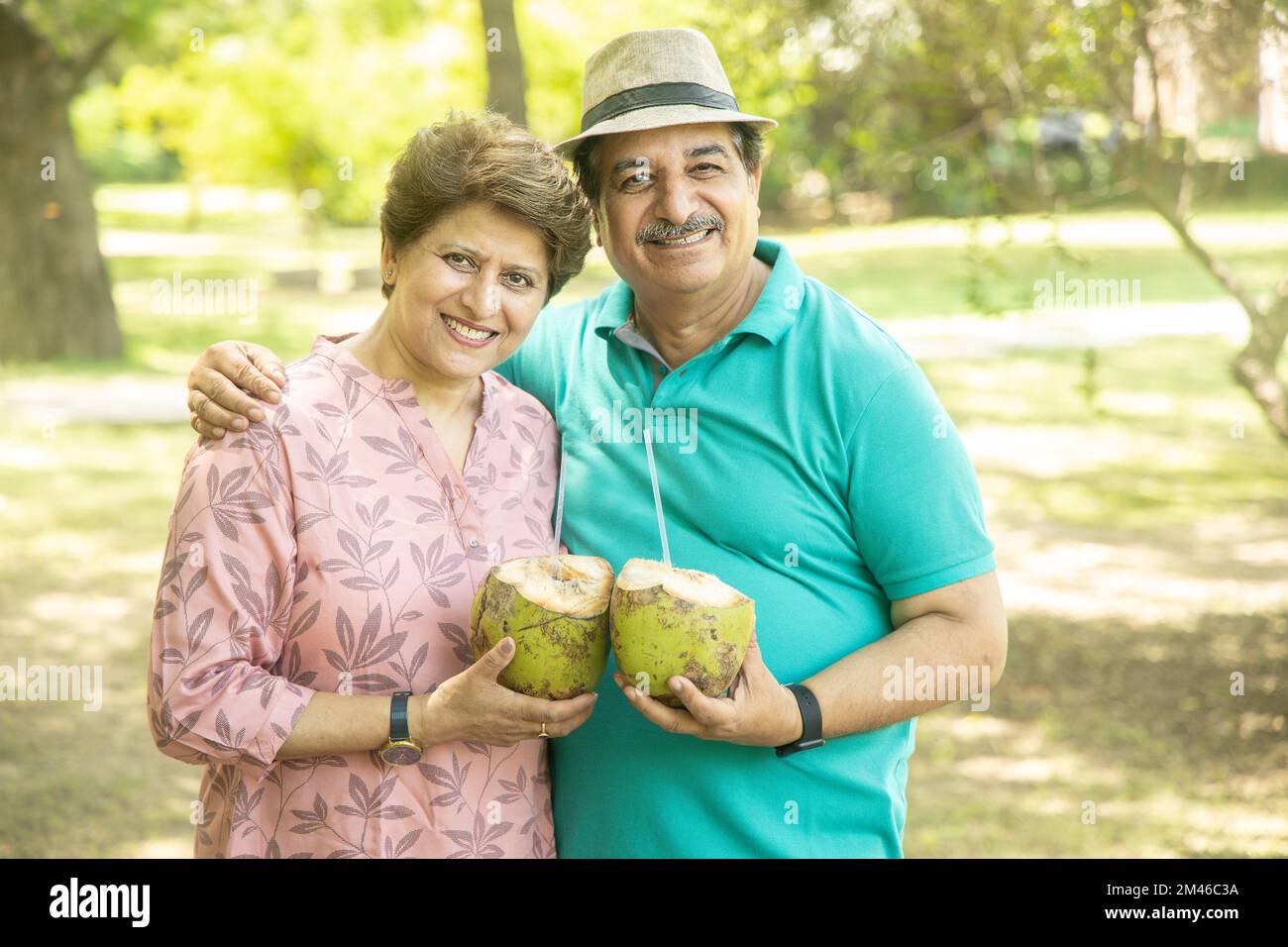 Felice coppia indiana senior con acqua di cocco al parco estivo. Anziani che godono di vita di pensione. Foto Stock