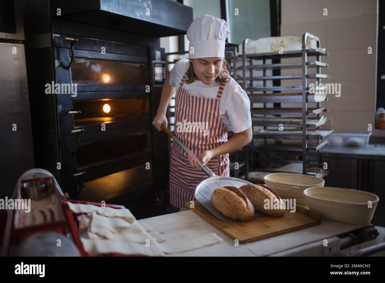 Buon panettiere giovane con pane fresco, in panetteria. Foto Stock