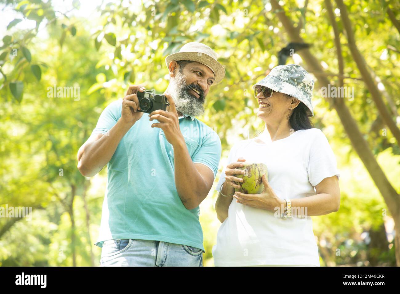 Felice coppia turistica anziana indiana in possesso di una fotocamera per scattare foto e vederle insieme al parco estivo. Persone mature in viaggio e vacanze. Foto Stock