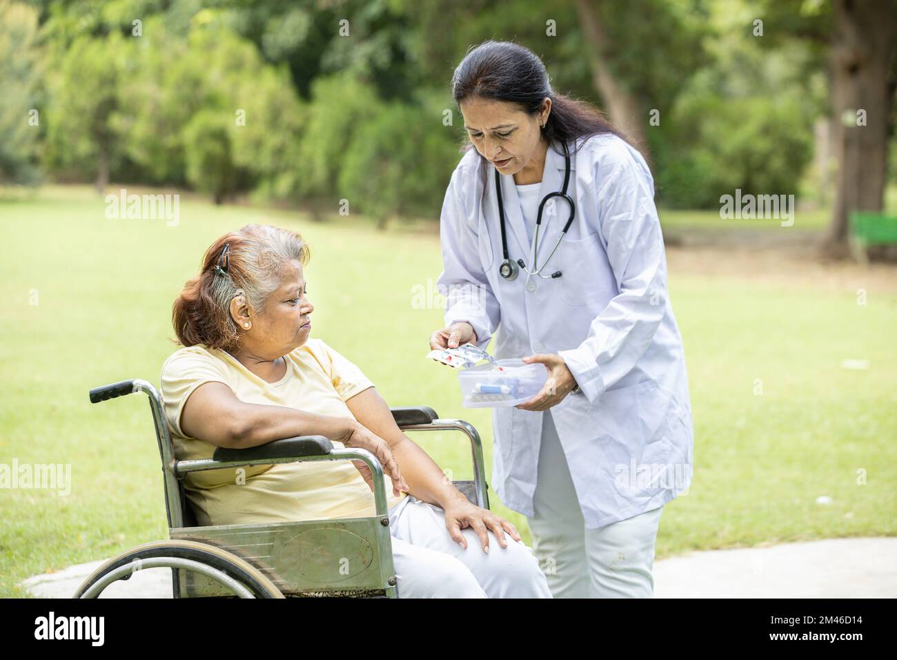 Medico indiano o infermiera dare medicina a pazienti anziani in una sedia a rotelle all'aperto nel parco. Foto Stock