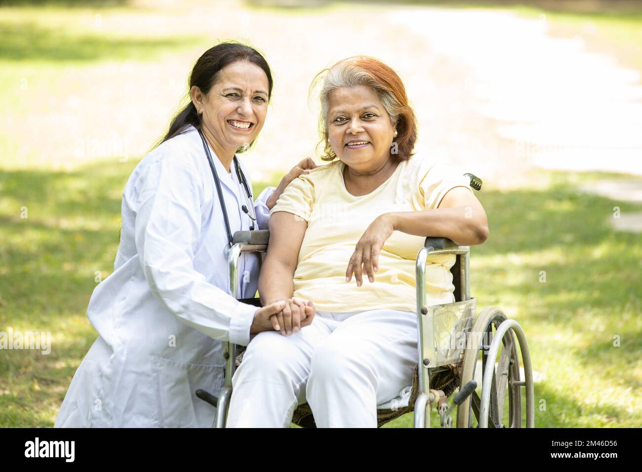 Ritratto di infermiera indiana caregiver con anziana paziente in sedia a rotelle all'aperto al parco, medico asiatico aiutare e sostenere anziani anziani anziani di età superiore Foto Stock