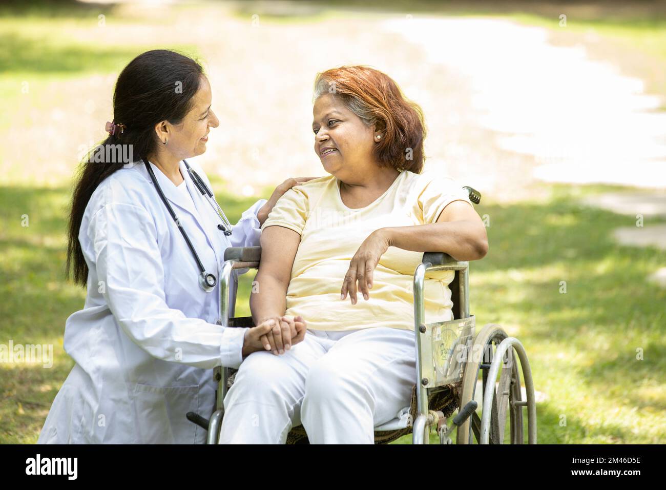 Infermiera indiana che si prende cura e parla con una paziente anziana in sedia a rotelle all'aperto al parco, medico asiatico aiutare e sostenere anziani maturi Foto Stock