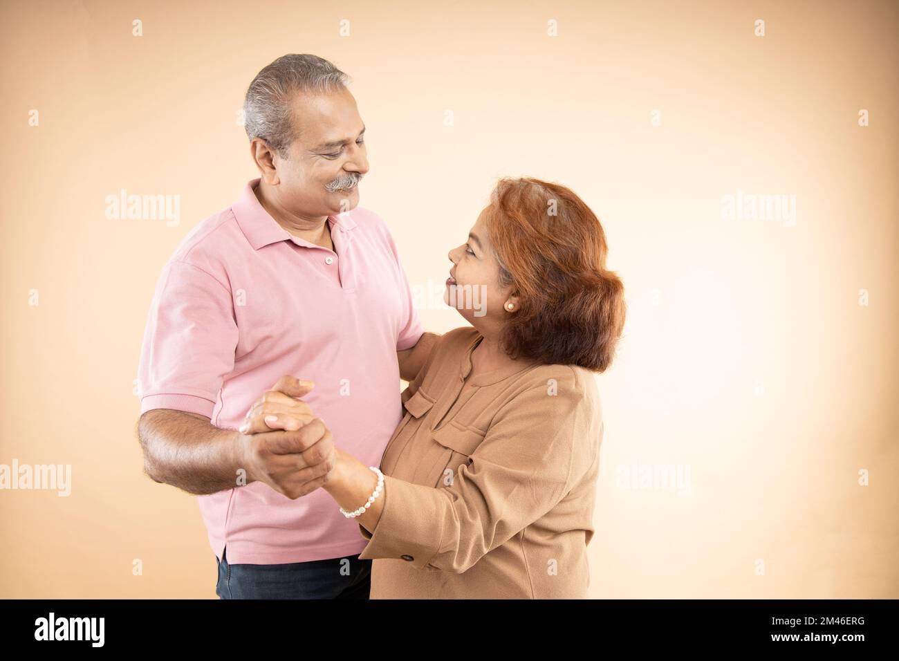 Felice coppia indiana senior in amore guardando l'altra mano mentre ballare insieme isolato su sfondo beige studio, due pensionati marito wif Foto Stock