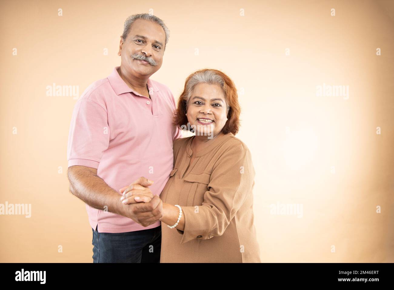 Felice coppia indiana senior in amore guardando l'altra mano mentre ballare insieme isolato su sfondo beige studio, due pensionati marito wif Foto Stock