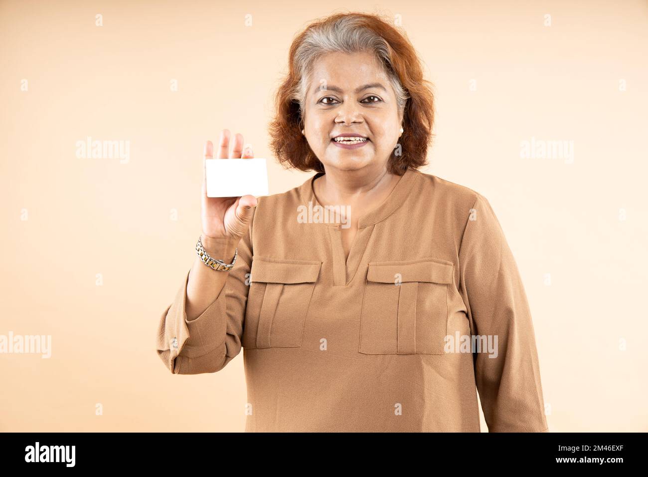 Donna indiana anziana felice che tiene in bianco business o carta di credito di debito in mano isolato su sfondo beige. Foto Stock