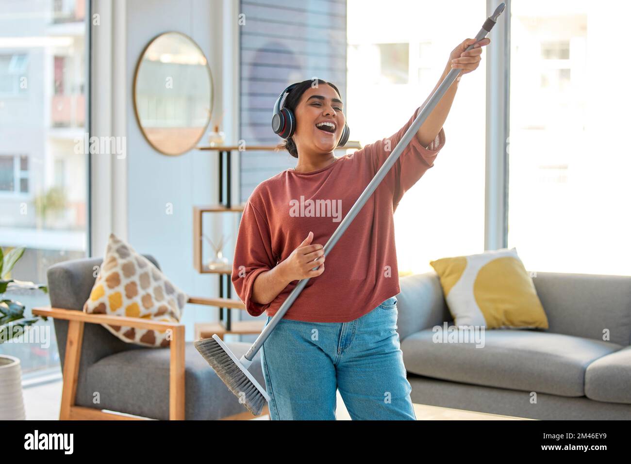 Danza, radio o donna pulizia con musica per cantare o ascoltare una canzone con scopa come una chitarra a casa. Relax, libertà o ragazza indiana felice Foto Stock