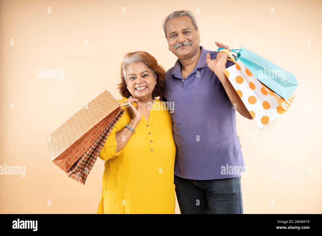 Coppia indiana anziana felice che tiene borse shopping in piedi insieme isolato su sfondo beige studio. la vita di pensione, le vendite e le offerte di e-commercio Foto Stock