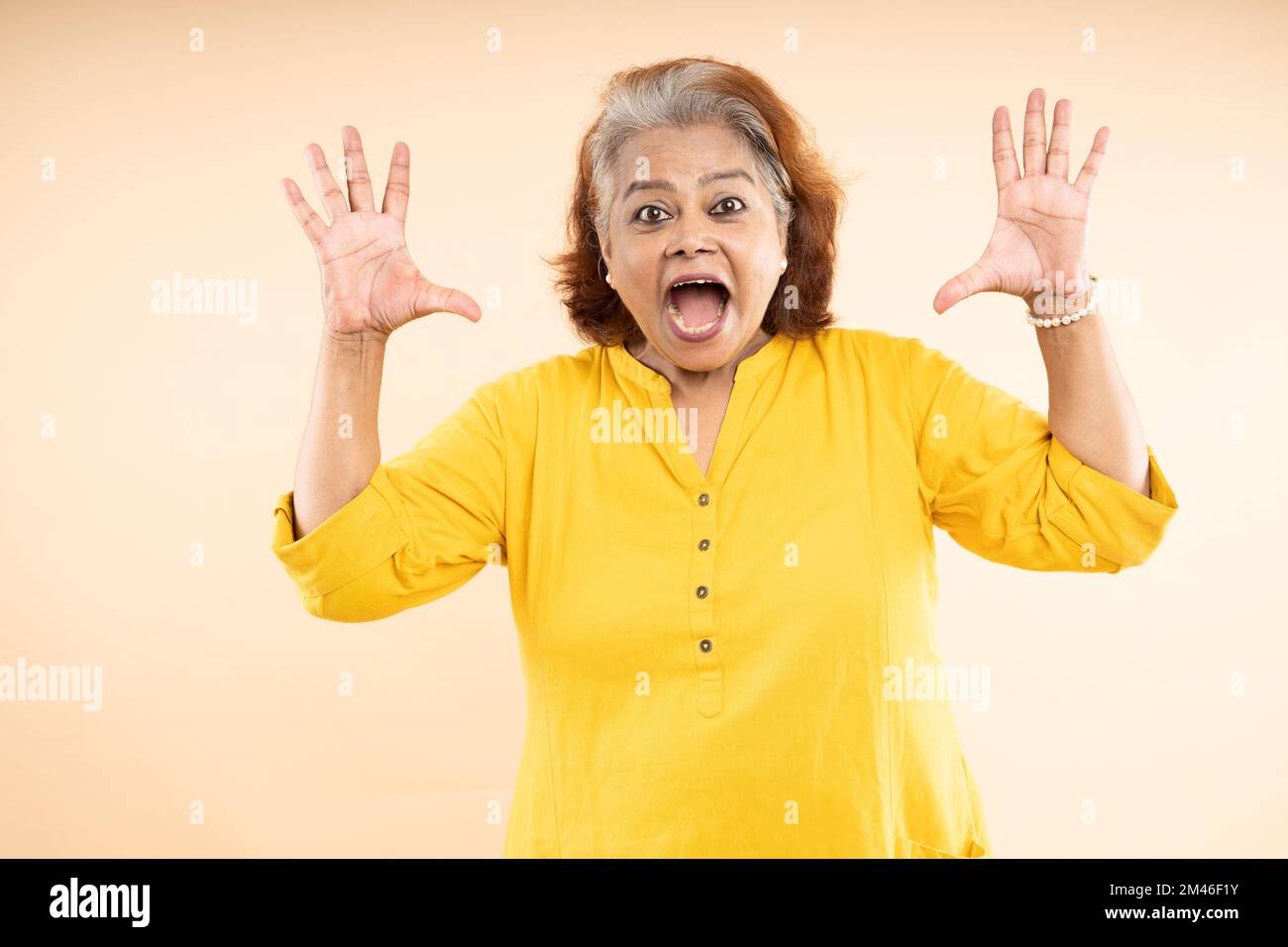 Urlando vecchia donna indiana anziana in piedi isolata su sfondo beige studio. Foto Stock