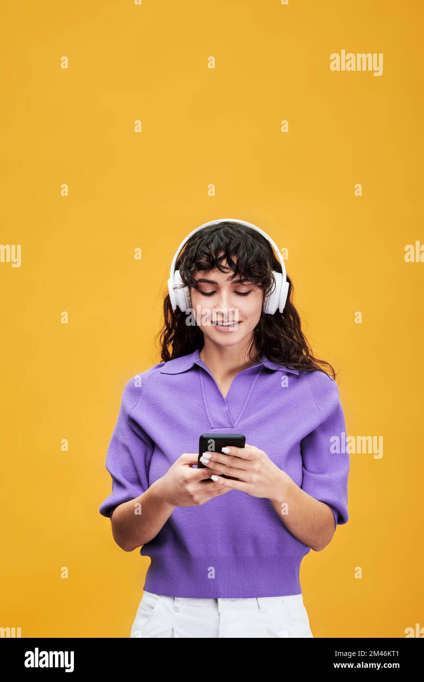 Bruna studentessa in cuffie che ascolta musica in pausa mentre scorre la playlist o guarda i video sullo smartphone Foto Stock