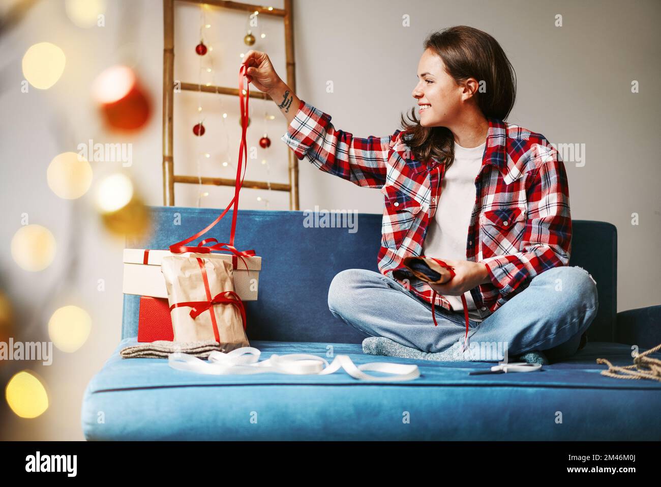 Giovane donna imballaggio regali di natale guardando il nastro rosso. Foto Stock
