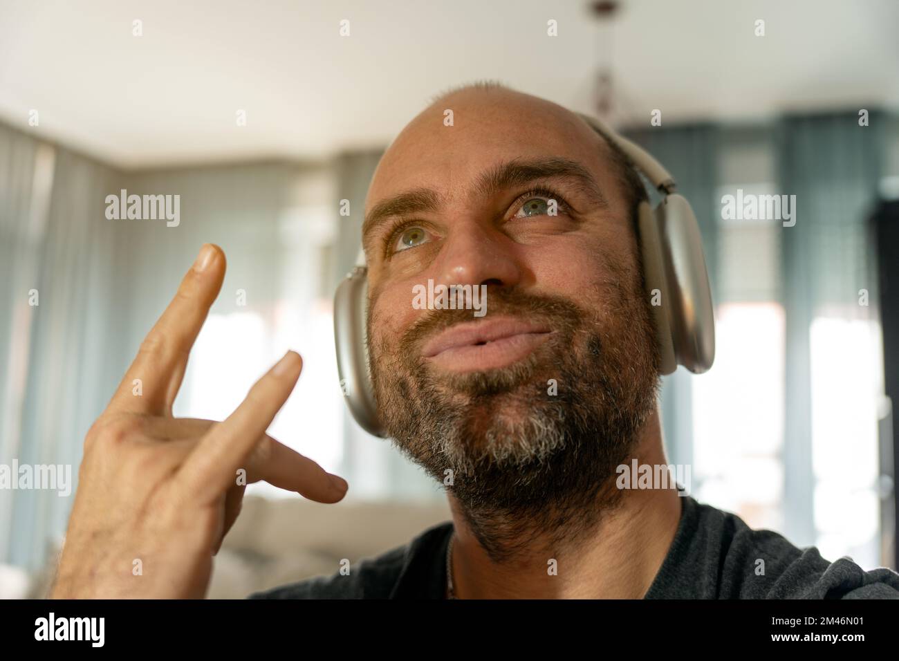 Uomo maturo che guarda con un sorriso e un rock sign mentre ascolta la musica preferita con le cuffie wireless a casa Foto Stock
