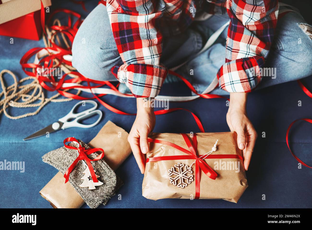 Vista ad angolo alto delle mani femminili e regalo di Natale in carta marrone artigianale e nastro rosso. Foto Stock