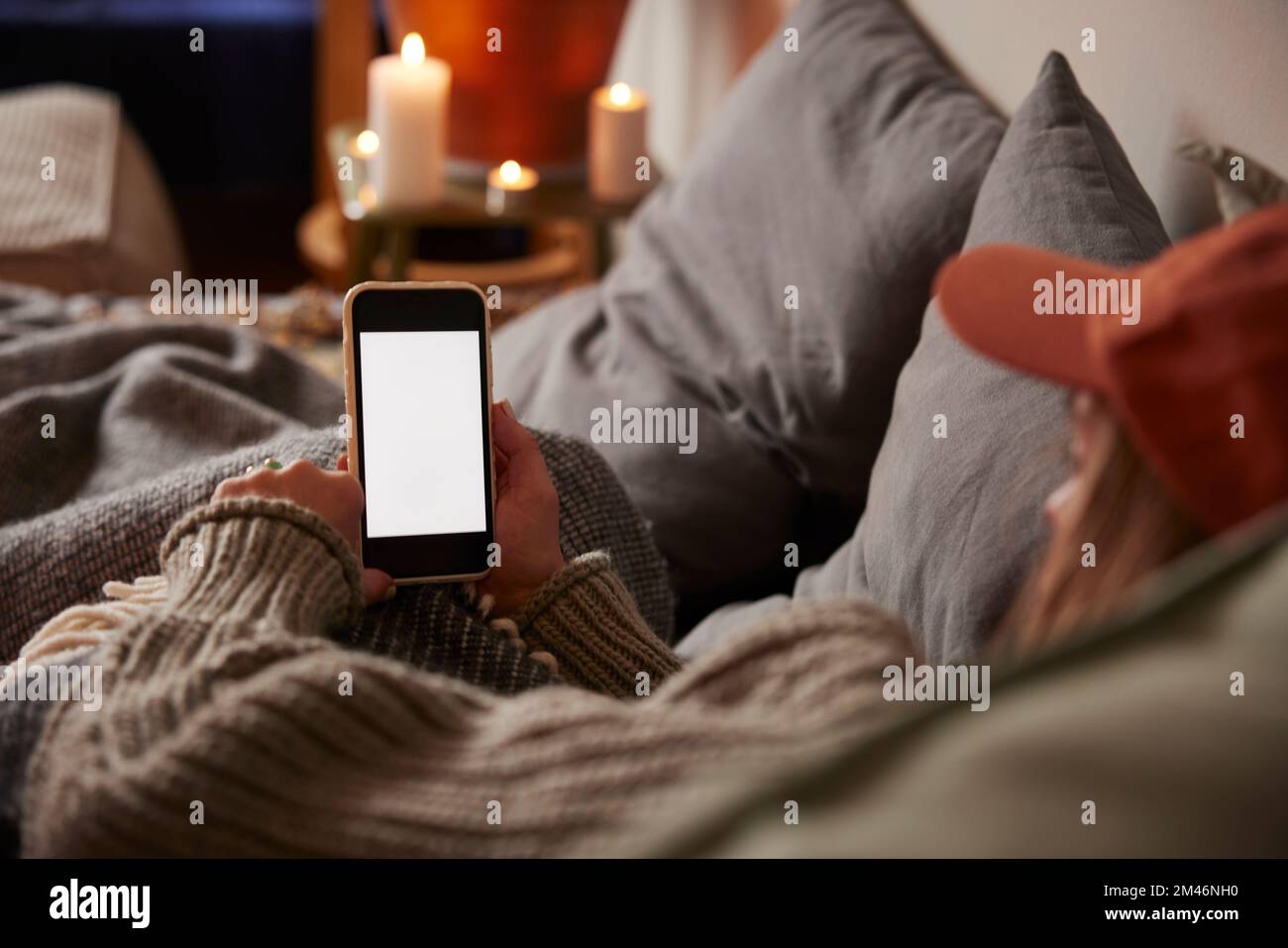 Donna sdraiata a letto e che usa il telefono Foto Stock