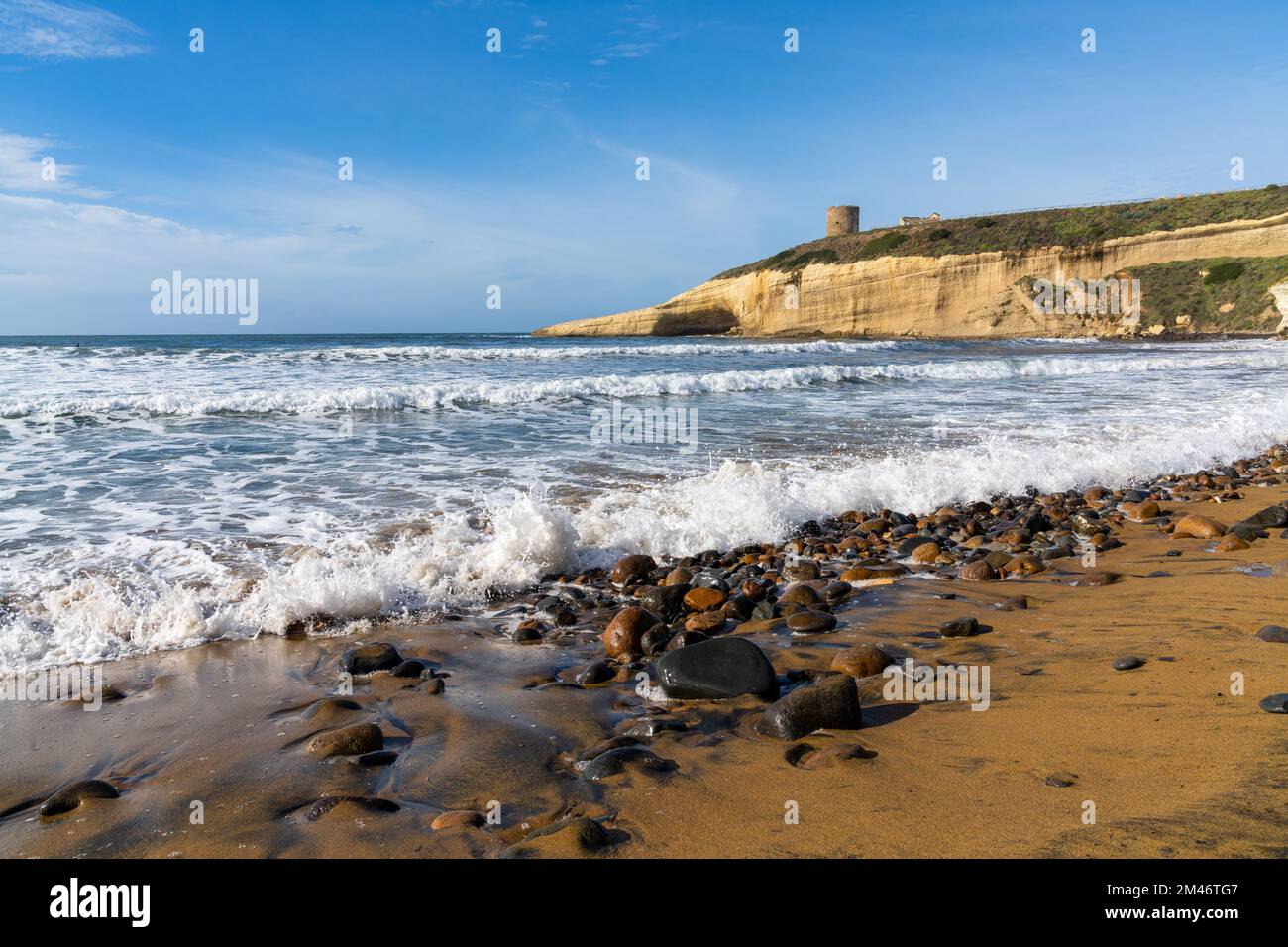 La spiaggia rocciosa e sabbiosa di Santa Caterina in Sardegna con la torre di avvistamento Pittinuri sulla scogliera alle spalle Foto Stock