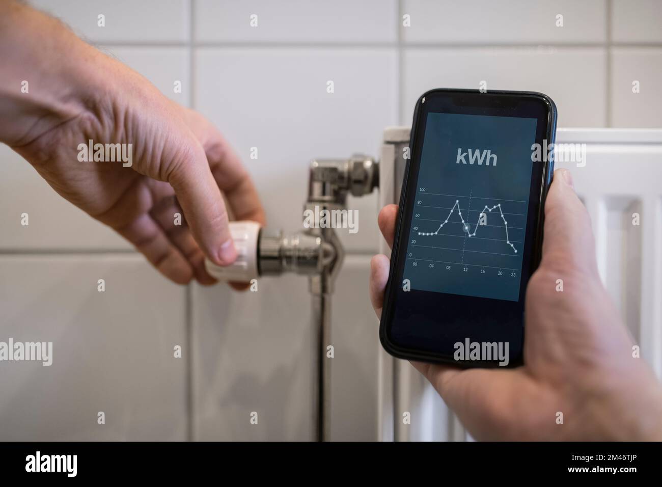 Persona che accende il termostato sul radiatore e controlla la tabella del consumo di energia sul telefono Foto Stock