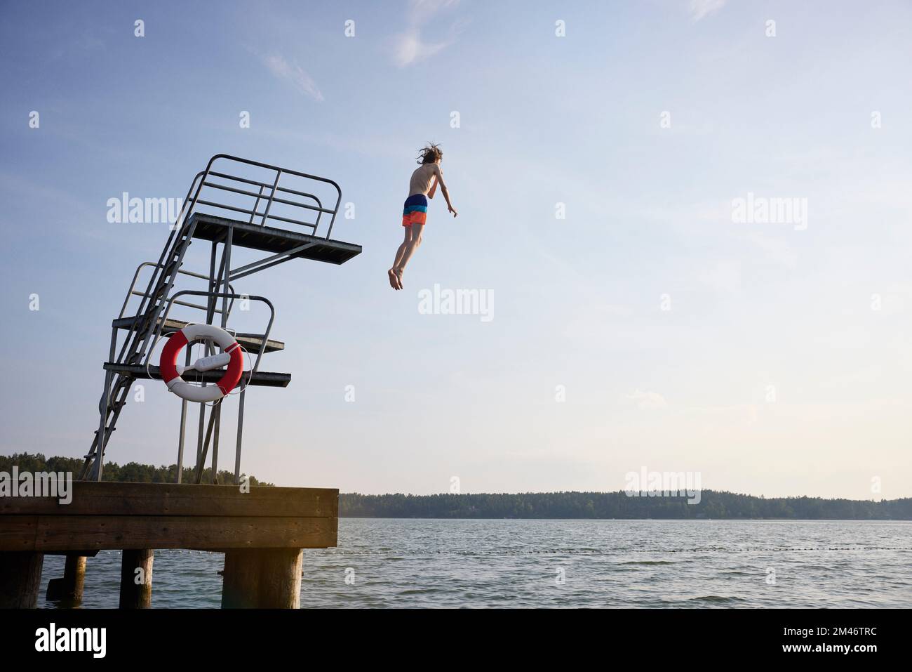 Ragazzo adolescente che salta in acqua dalla torre di salto Foto Stock