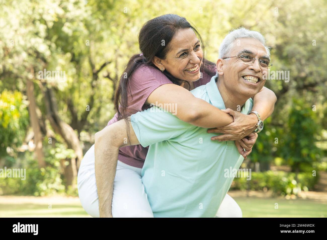 Coppia anziana indiana felice godendo la vita divertirsi al parco estivo, l'uomo che dà piggyback corsa a donna. Foto Stock