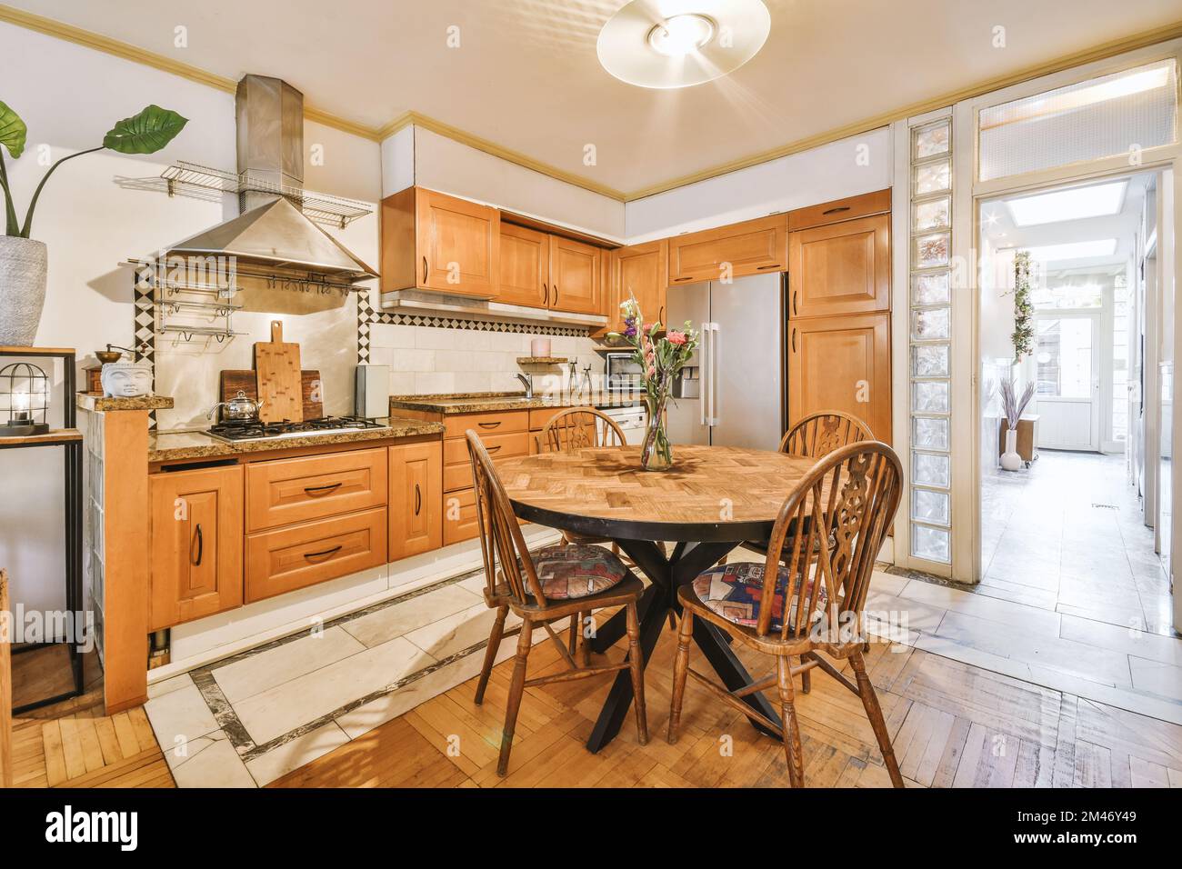 una cucina e zona pranzo in una casa con pavimenti in legno duro, armadi in legno, pareti bianche e una porta aperta che conduce al patio Foto Stock