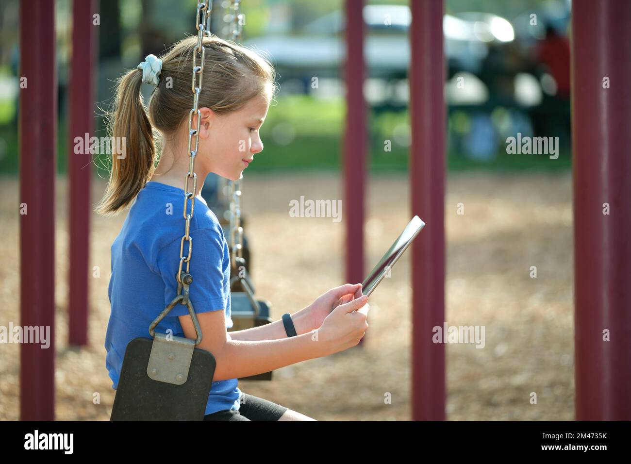 Ragazza felice bambino che utilizza un tablet digitale per giocare a videogame durante le vacanze estive seduto sul swing nel parco Foto Stock