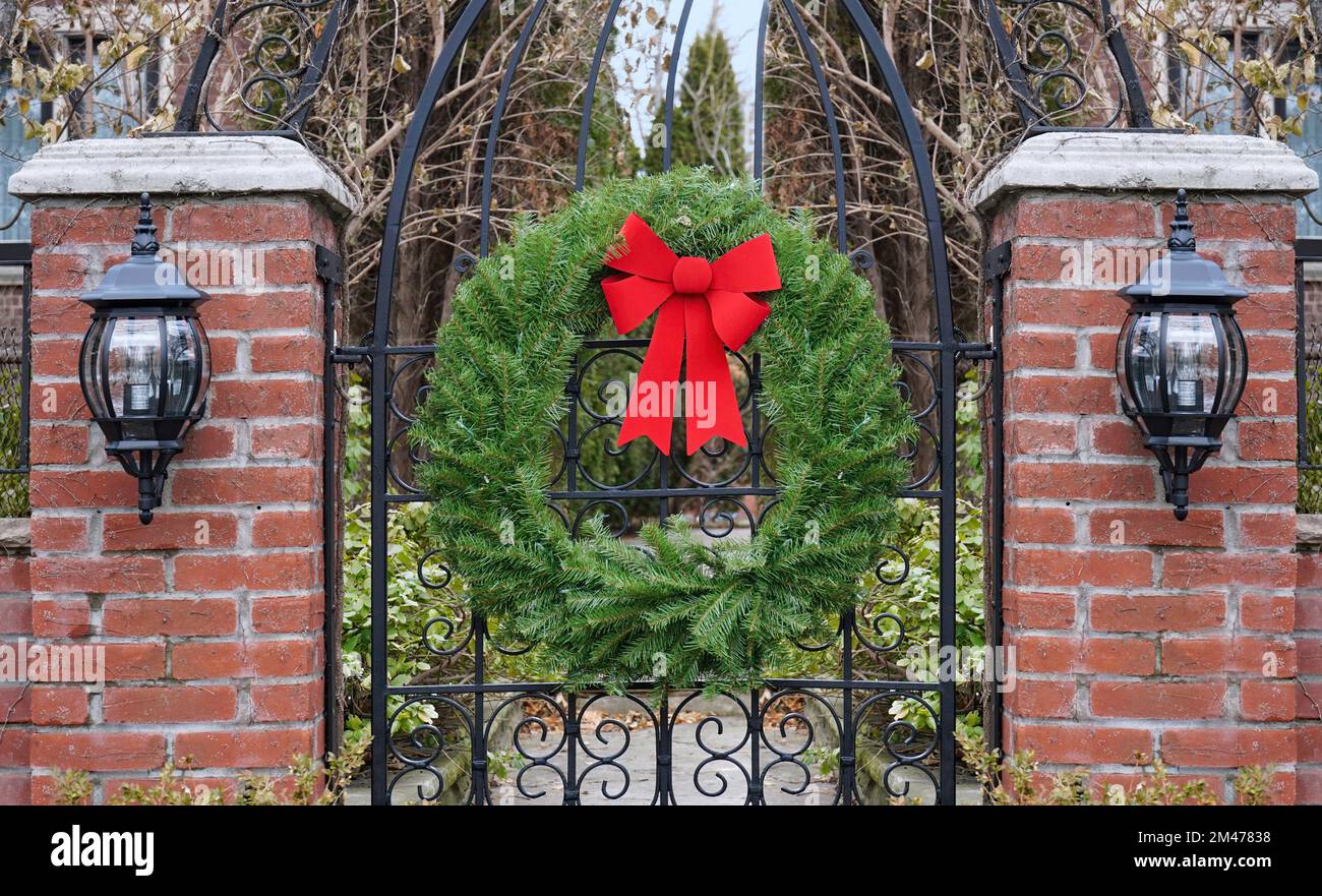 Cancello da giardino con colonne in mattoni decorate con corona di Natale con rami di pino e arco rosso Foto Stock