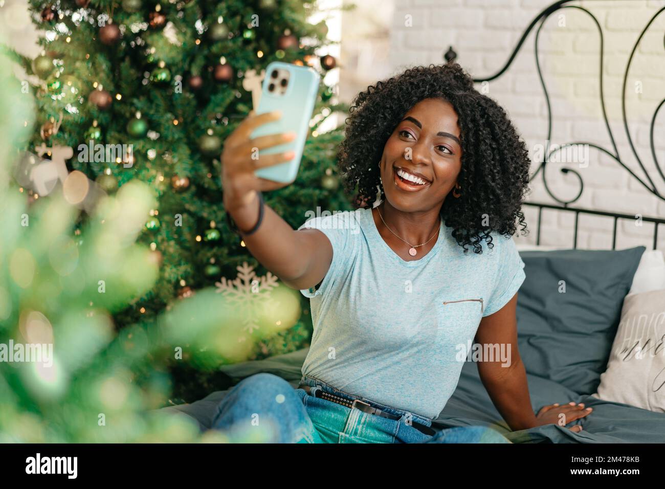 Felice donna nera che usa lo smartphone in una stanza decorata per Natale Foto Stock