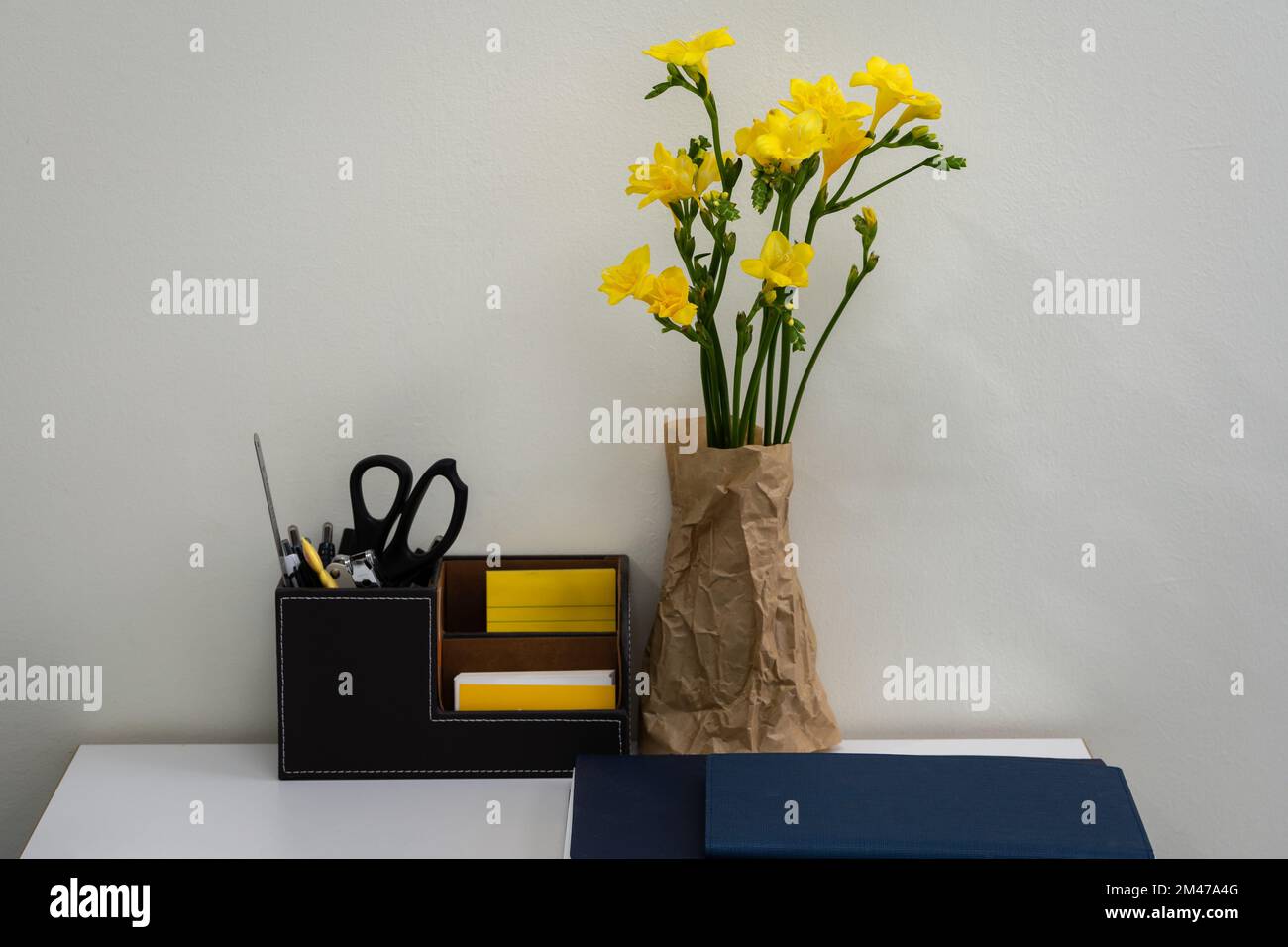 Una custodia a matita e porta biglietti da visita e un vaso freesia stand alla fine della scrivania.sfondo bianco parete. area di lavoro Foto Stock