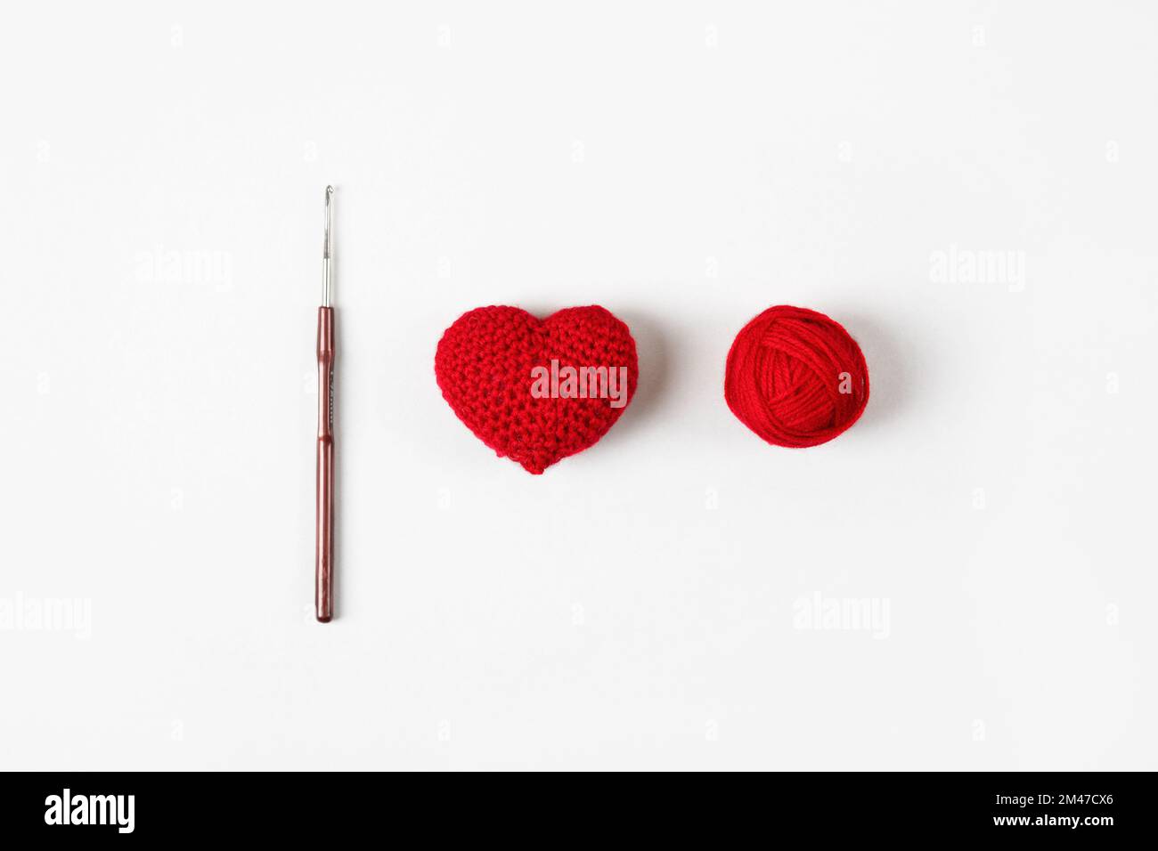Cuore rosso arroccato su fondo grigio e una palla di filo con un gancio. San Valentino, simbolo dell'amore. Foto Stock
