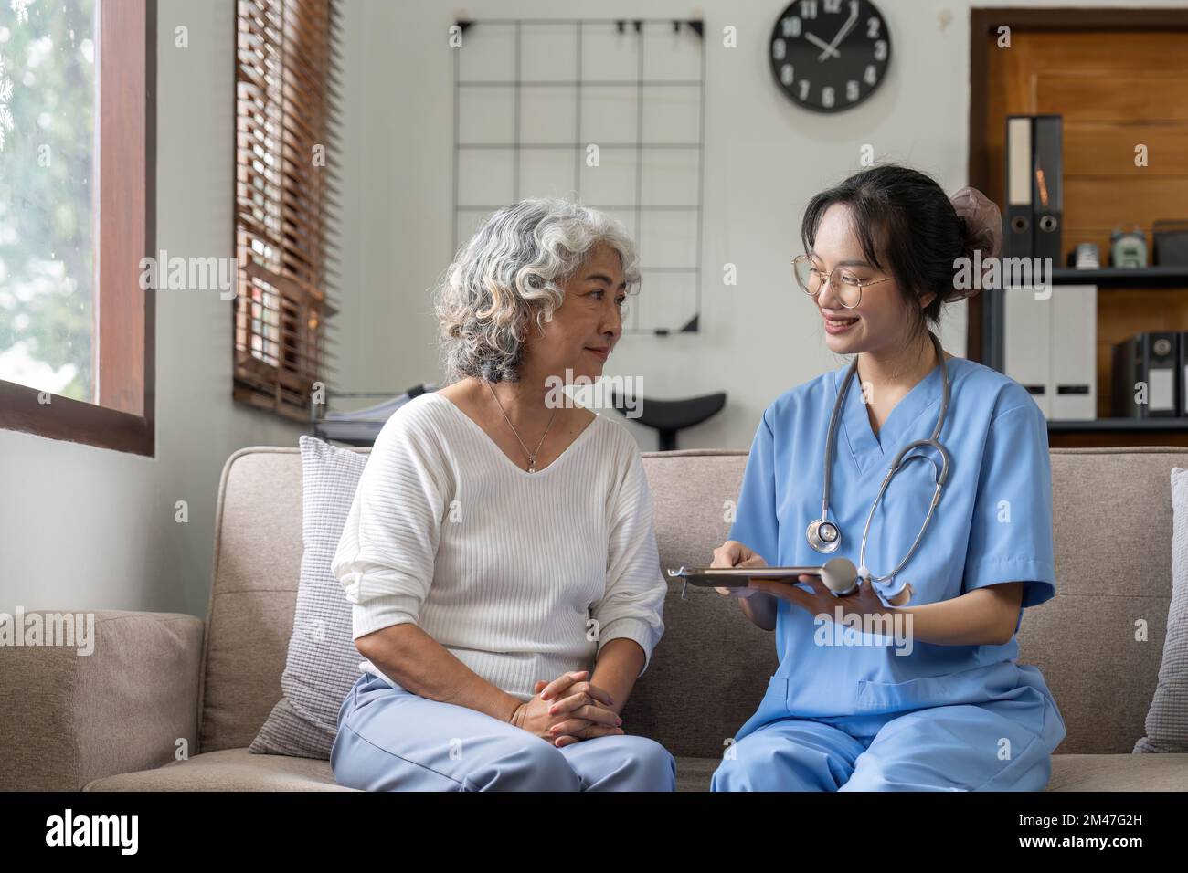 Operatore sanitario o caregiver che visita una donna anziana in casa, spiegando il dosaggio della medicina Foto Stock