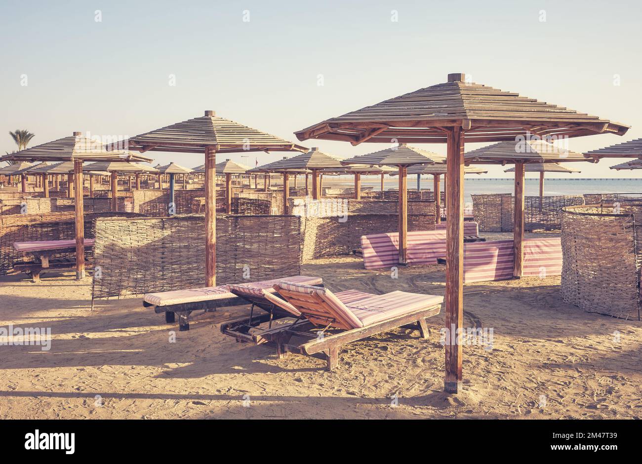 Foto dai toni retrò di lettini e ombrelloni in legno su una spiaggia tropicale. Foto Stock