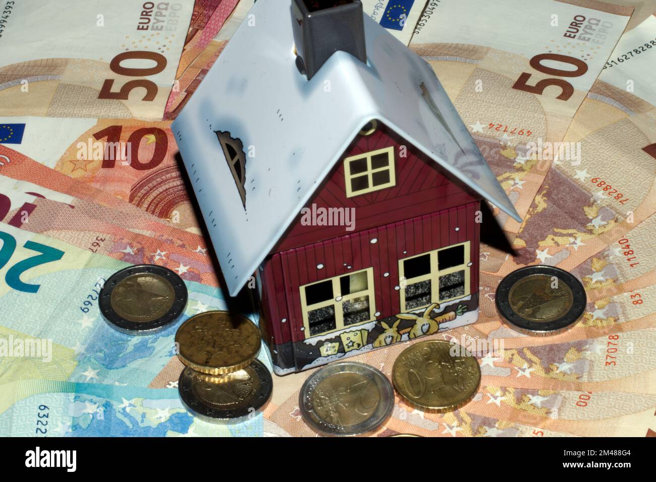 Symbol immagine prezzi immobiliari. Modello di una casa su banconote e monete Foto Stock