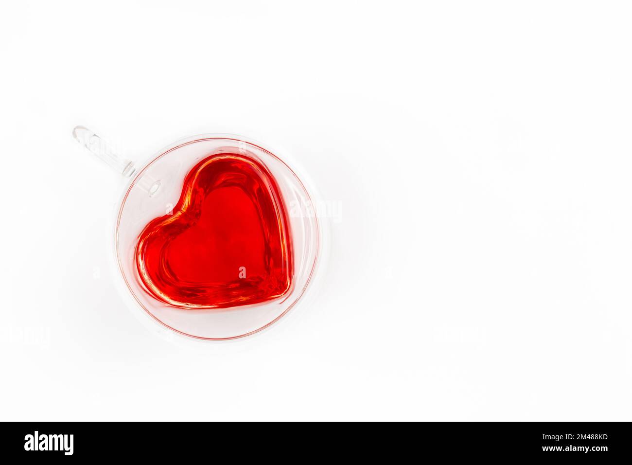 Una tazza trasparente a forma di cuore con tè su sfondo bianco, piatto. Foto Stock