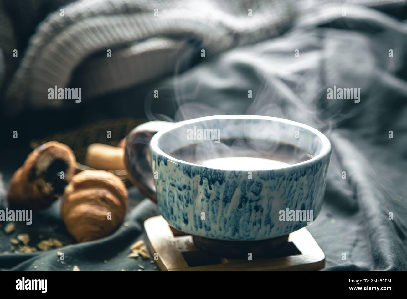 Una tazza di tè caldo e croissant su uno sfondo sfocato a letto. Foto Stock
