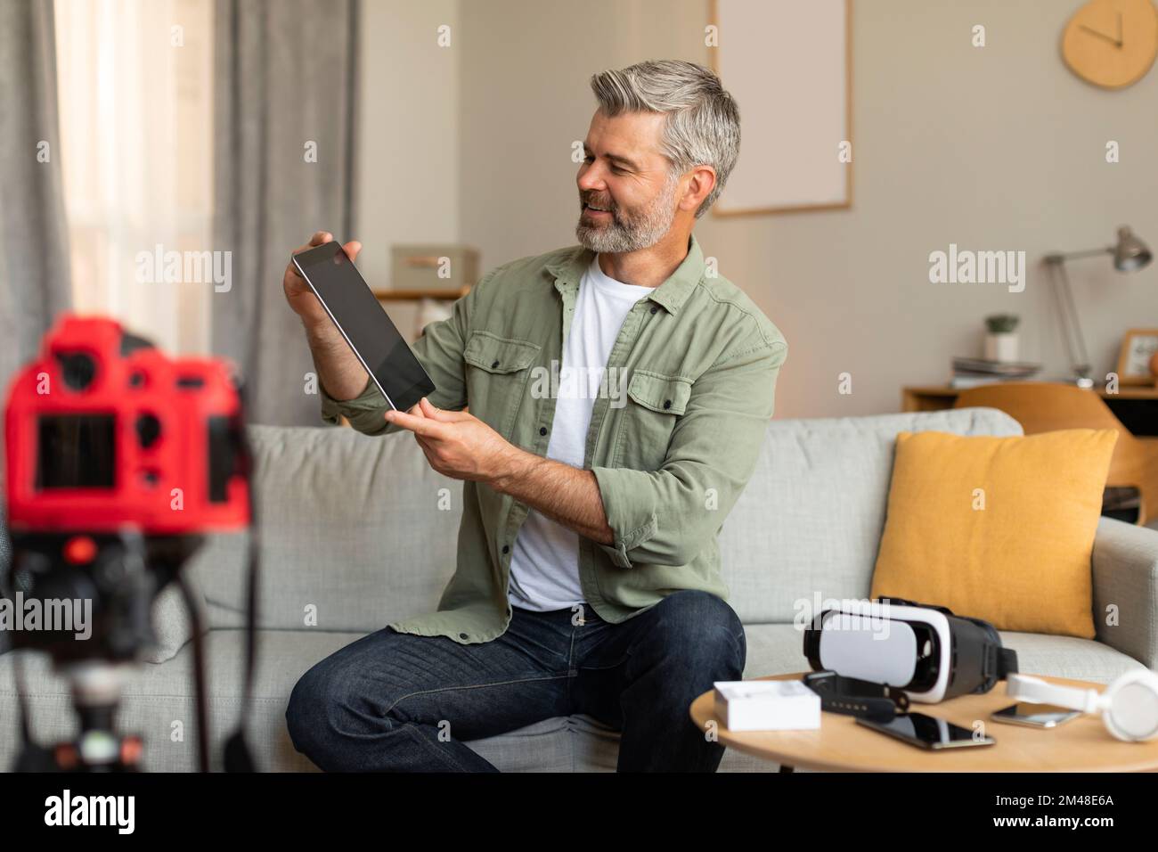 Lavoro moderno e hobby. Sorridente uomo maturo caucasico blogger sparare video blog, guardando tablet Foto Stock