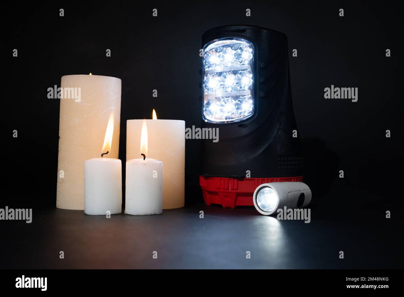 Torce elettriche e candele accese su sfondo nero, fonti alternative di luce e calore Foto Stock