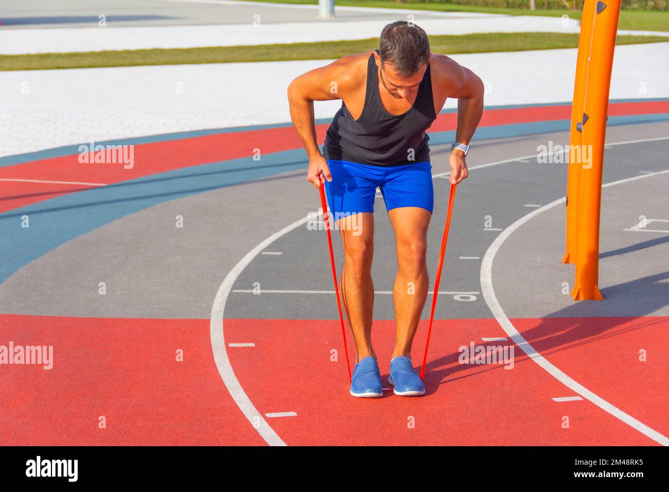 L'uomo sta allenando le mani e la schiena con fasce elastiche. Tipo che si esercita con la gomma che si steppa su una fascia di gomma. Forma, fitness, esercizio fisico, allenamento e salute Foto Stock