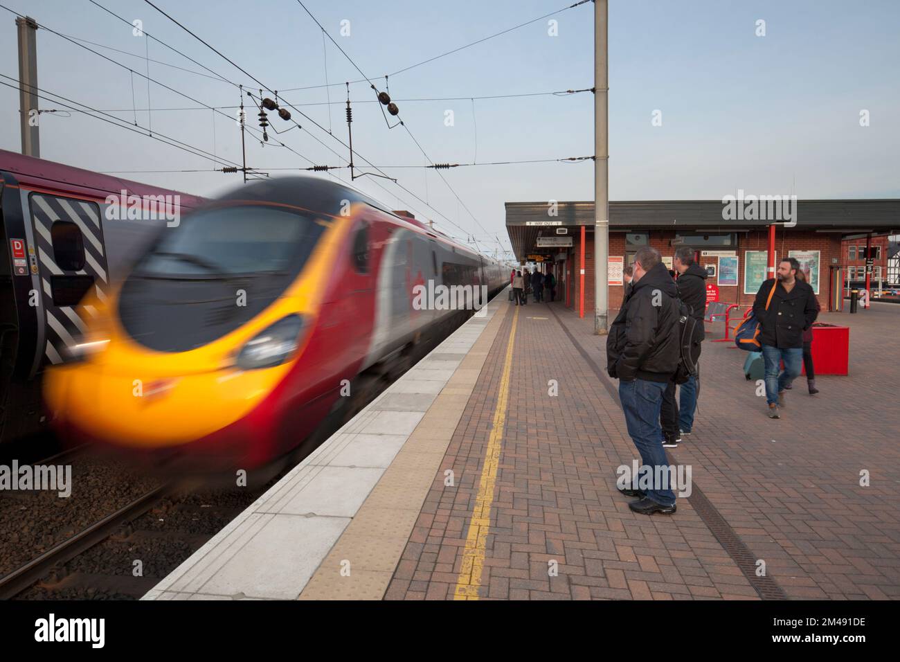 Virgin Train arrivo alla stazione ferroviaria di Wigan North Western con i passeggeri in attesa sulla piattaforma della stazione ferroviaria dietro la linea gialla Foto Stock