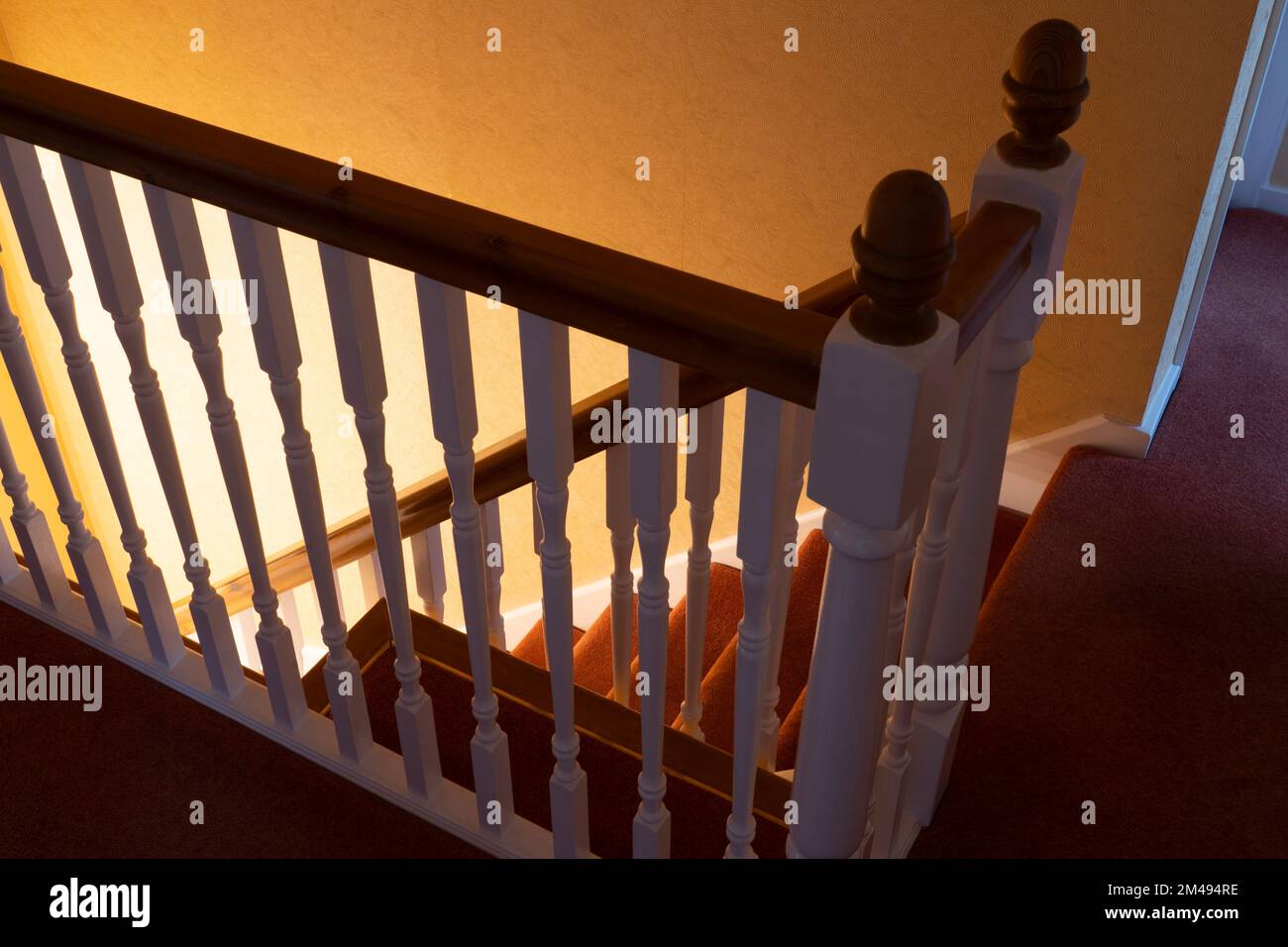 Inghilterra casa interno, atterraggio guardando verso il basso attraverso ringhiere su scale tappezzate con una luce brillante sotto Foto Stock
