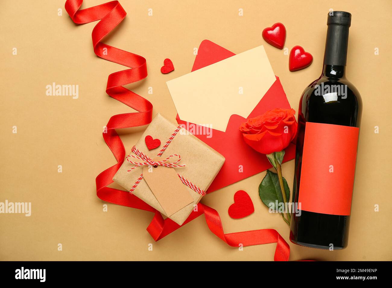 Lettera bianca con rosa, bottiglia di vino, regalo e cuori su sfondo beige. Festa di San Valentino Foto Stock
