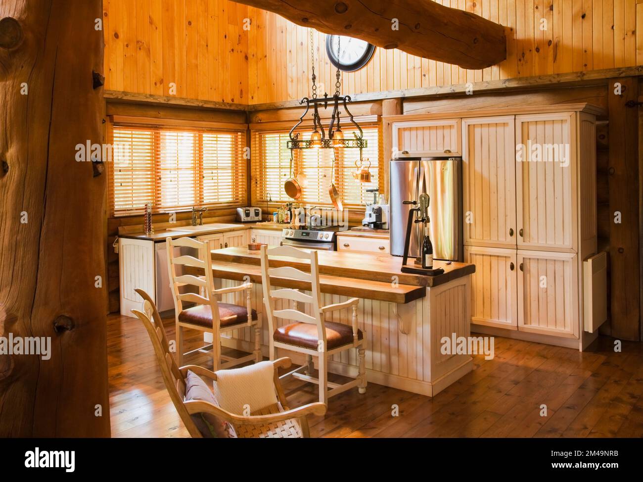Isola in legno colorato con latticello con piano in legno di pino e alto schienale sedile in pelle poltrone in legno in cucina all'interno di casa in tronchi. Foto Stock