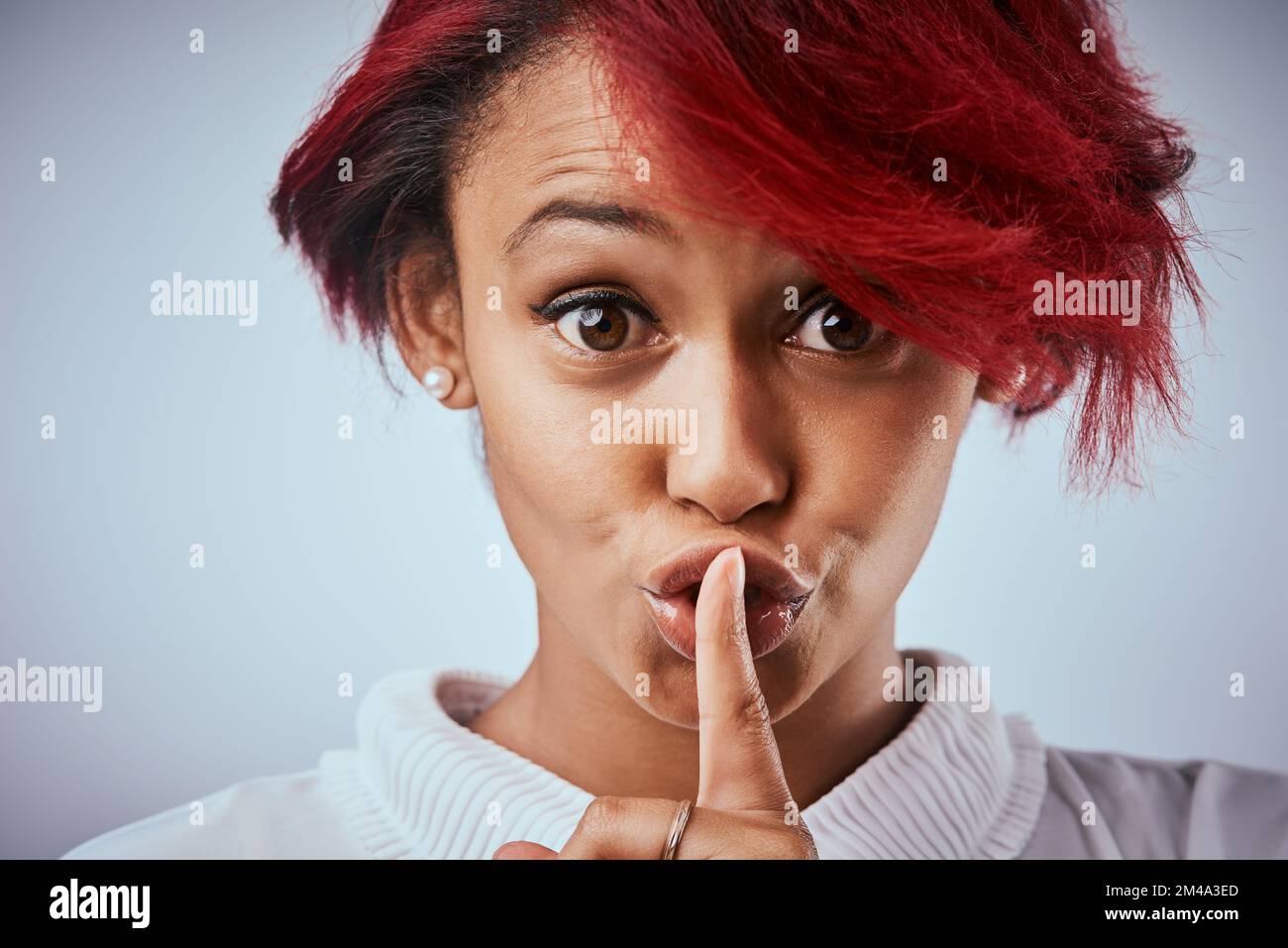 Se non potete essere gentili, Fai silenzio. una bella giovane donna che posa con il dito sulle labbra su uno sfondo grigio. Foto Stock